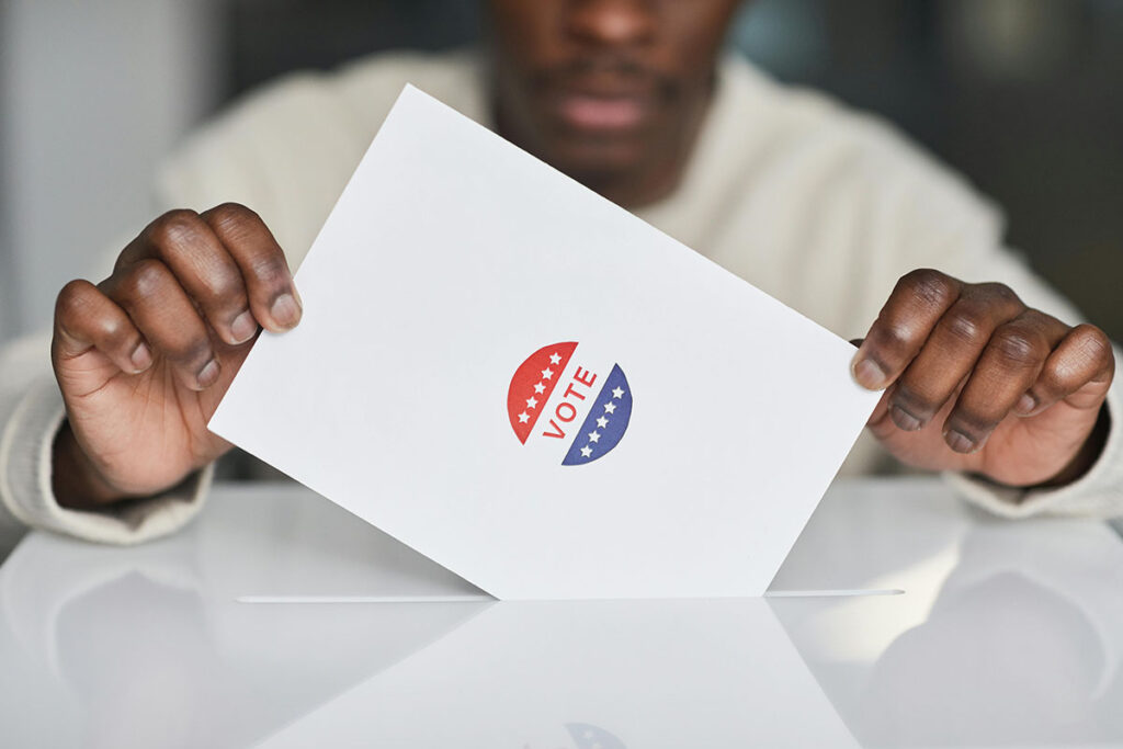 black voter dropping a voting ballot into a white box.